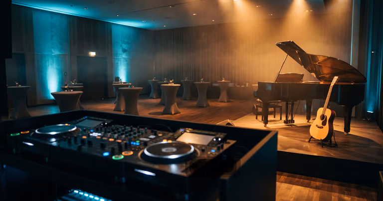 DJ-Pult im Vordergrund, dahinter beleuchtete Bühne mit Klavier und Gitarre